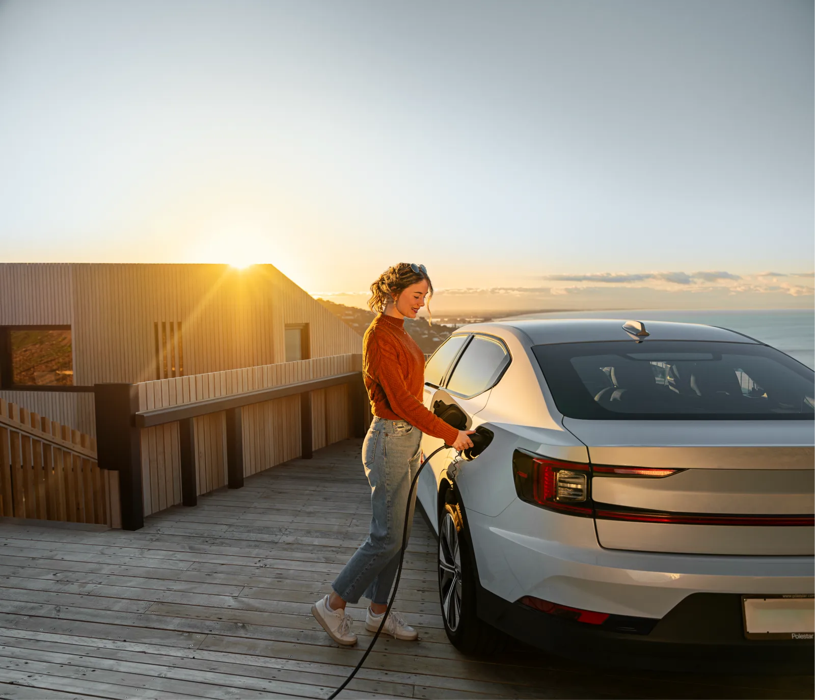 Woman plugging Evnex charger into electric vehicle at a coastal property at sunset