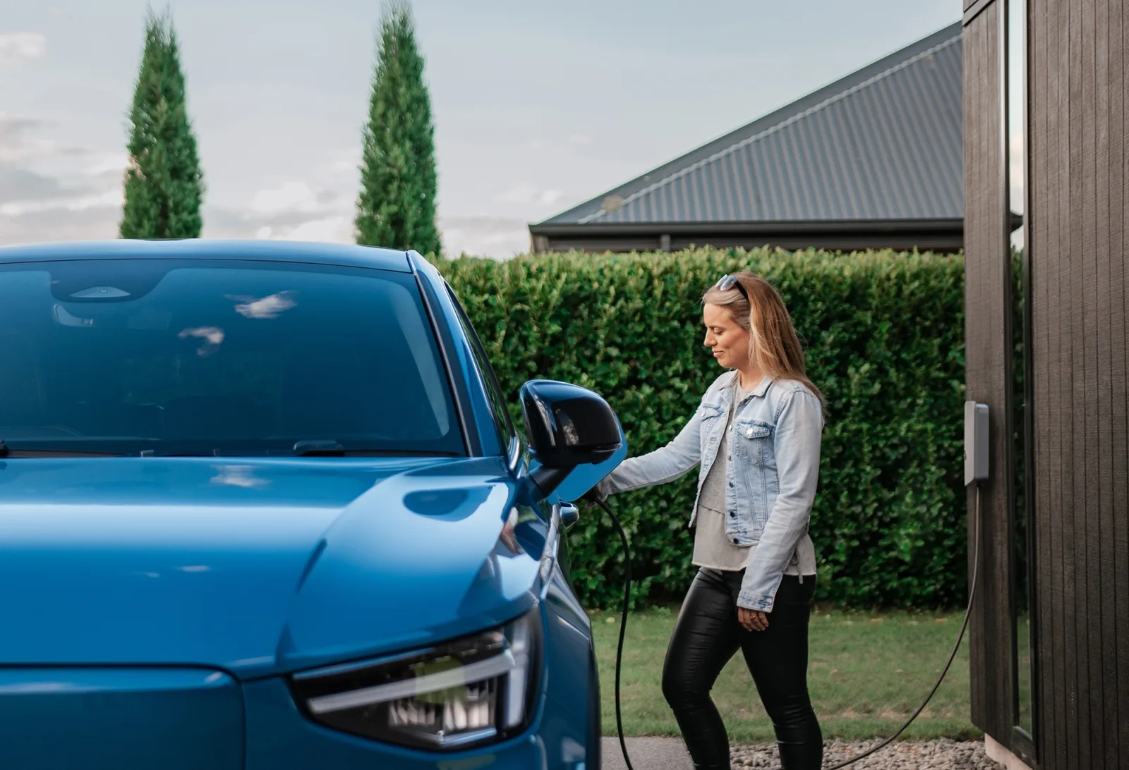 Woman charging her blue electric vehicle in a New Zealand driveway with Evnex charger
