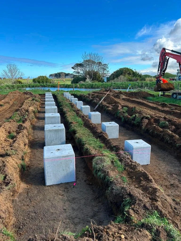 Rows of engineered concrete foundations set in trenches for a ground-mounted solar array on a Taranaki farm