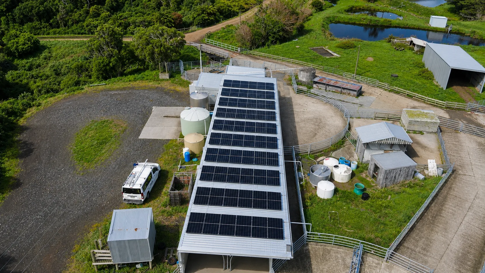 Aerial view of solar panels on a dairy shed roof with yards, silos and paddocks beyond